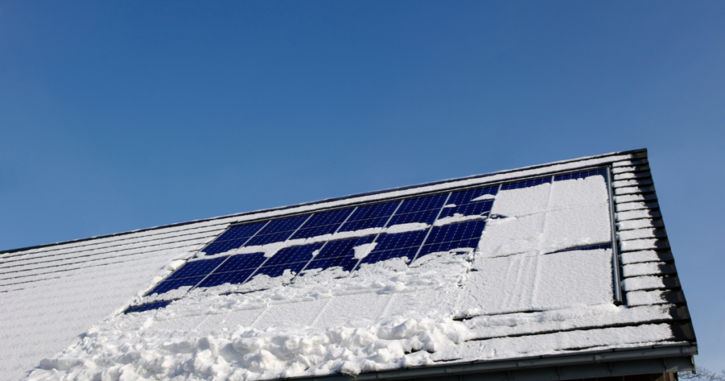 A close-up of a house’s rooftop with solar panels partially covered by snow, illustrating solar energy production in winter conditions.