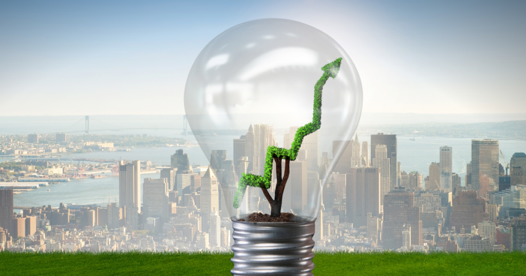 A large transparent lightbulb with a small tree inside, shaped like an upward-trending arrow covered in green foliage. The background features a city skyline with a river and a suspension bridge, symbolizing sustainable energy and economic growth.
