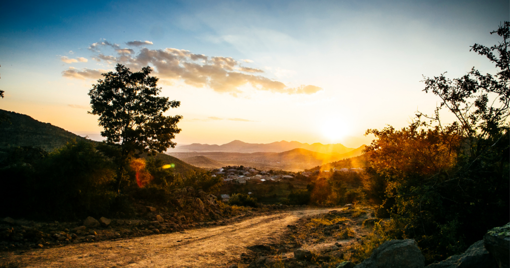 A nature trail with the sun rising behind the mountainscape.