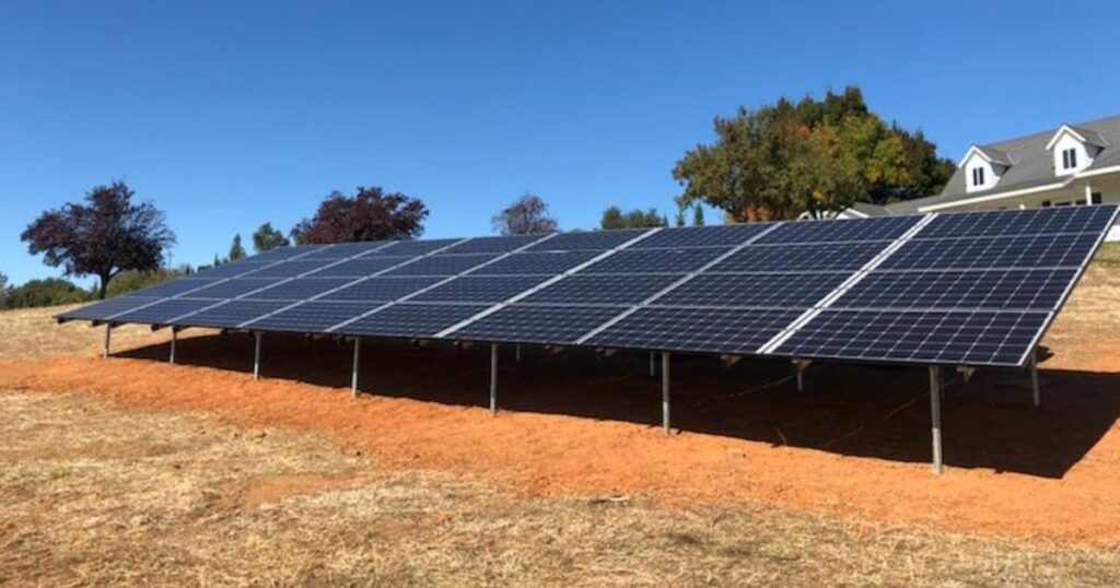 A solar installation built to take advantage of the 2025 solar tax credits, there is red dirt underneath and blue sky plus oak trees in the background.